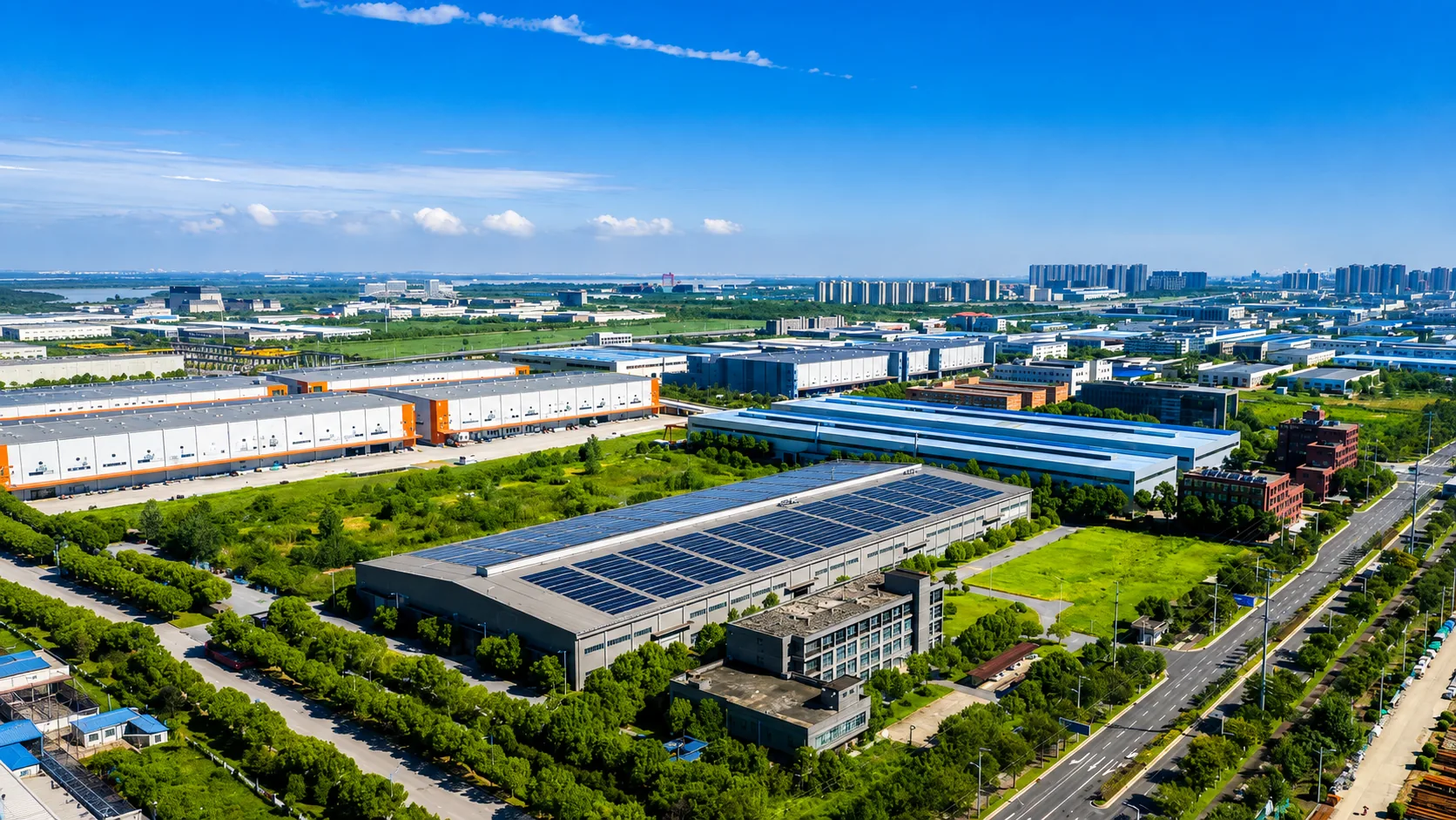 Aerial view of a solar-powered industrial park with rooftop solar panels, warehouse buildings and green landscape under a bright blue sky