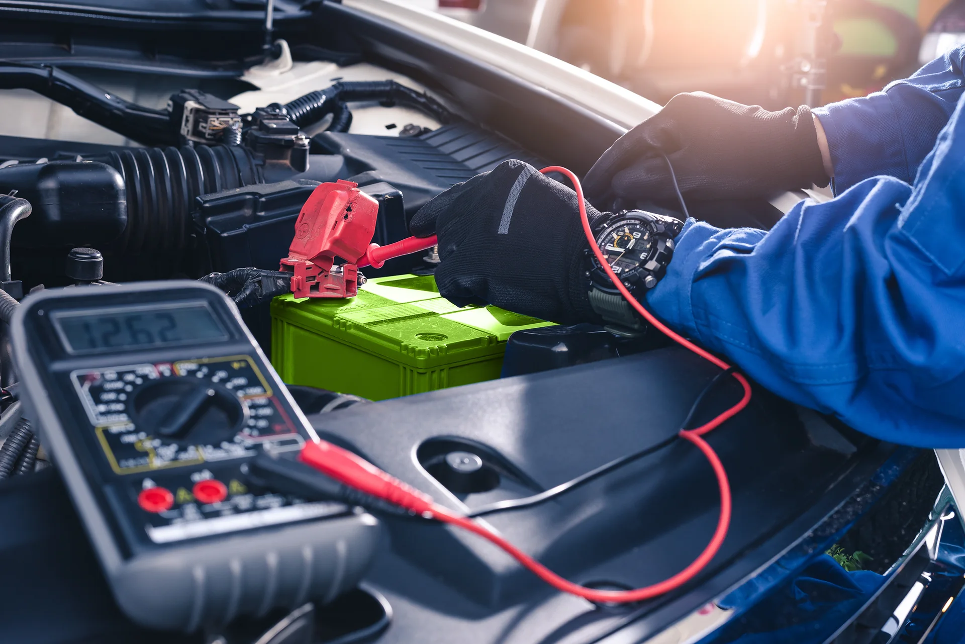 Technician testing a car battery with a multimeter during automotive battery service